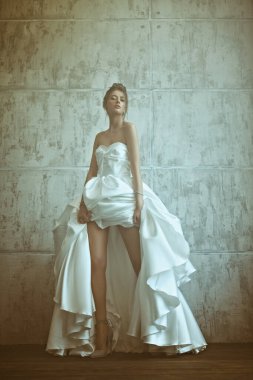 Lüks bir gelinlik içinde, stüdyoda grunge arka planda poz veren güzel bir mankenin tam boy portresi. Düğün modası.