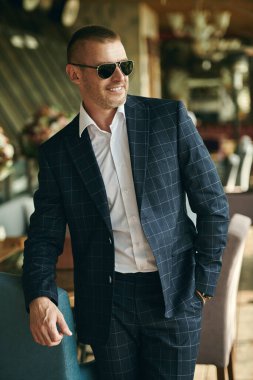 Zarif klasik takım elbiseli yakışıklı olgun bir adam yaz terasında dinleniyor. Erkek modası. Optik, erkekler için güneş gözlüğü. Yaz tatili.