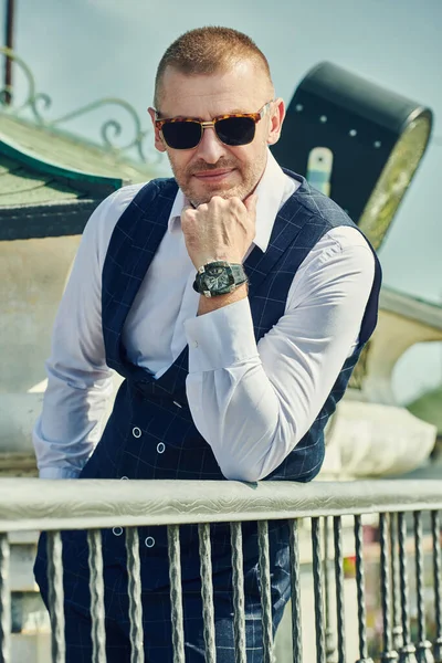 Happy handsome mature man in an elegant classic suit having a rest on the summer terrace. Men\'s fashion. Optics, sunglasses for men. Summer vacation.