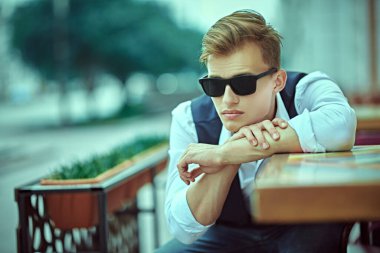 Kafenin verandasında poz veren yakışıklı bir genç adamın portresi. Yaz modası. Yaz tatili ve tatil.