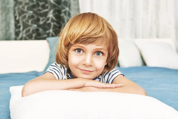 Joyful funny kid lying on a bed and smiling at camera. Happy childhood. Family at home.