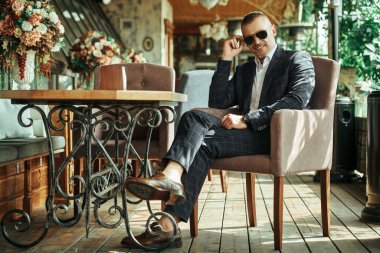 Zarif klasik takım elbiseli yakışıklı olgun bir adam yaz terasında dinleniyor. Erkek modası. Optik, erkekler için güneş gözlüğü. Yaz tatili.