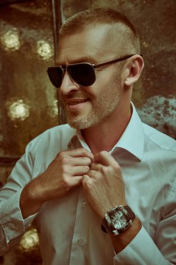 Lüks bir dairede, beyaz gömlekli ve modern güneş gözlüklü, çok zengin bir adamın portresi. Erkek güzeli, moda. Optik, erkekler için güneş gözlüğü..