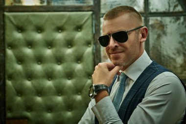 Lüks bir dairede duran şık takım elbiseli, olgun, yakışıklı bir adamın portresi. Erkek güzeli, moda. Optik, erkekler için güneş gözlüğü..