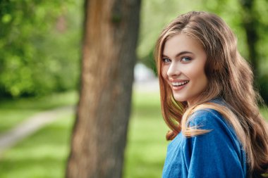 Parkta kameraya gülümseyen güzel mutlu bir kızın portresi. Yaz tatili.