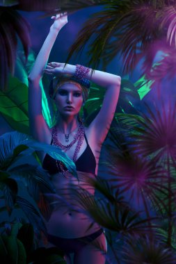Islak saçlı güzel ateşli kadın tropikal bitkilerin arasında duruyor. Güzellik, moda ve kozmetik konsepti. Tropikal ülkelerde tatil.