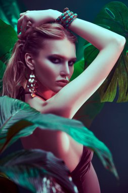 Islak saçlı güzel ateşli kadın tropikal bitkilerin arasında duruyor. Güzellik, moda ve kozmetik konsepti. Tropikal ülkelerde tatil.