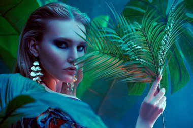 Palmiye yapraklarının arasında ıslak saçlı güzel bir tropikal kadının portresi. Güzellik, moda ve kozmetik konsepti. Tropikal ülkelerde tatil.