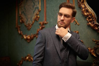 Zarif takım elbiseli yakışıklı zengin adam lüks dairelerde duruyor. İş adamı portresi. Erkek modası..
