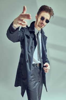 Zarif siyah takım elbiseli, beyaz gömlekli ve güneş gözlüklü, gri arka planda, pencere gölgeli modern tarz bir adam. Erkek modası.