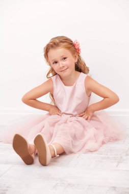 Beyaz bir odada yerde oturan sevimli küçük bir kızın portresi. Stüdyo çekimi. Mutlu çocukluk. 