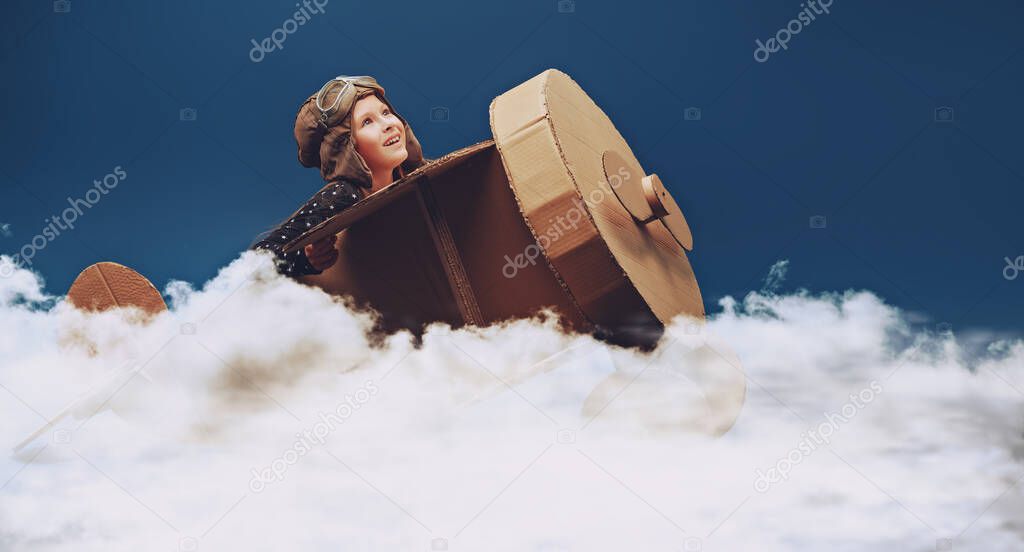 Cute dreamer girl playing with a cardboard airplane. Childhood. Fantasy, imagination. Studio portrait on a dark blue background.