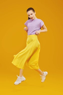 Parlak elbiseli manken sarı arka planda hareket halinde stüdyoda poz veriyor. Moda, yeni yaz tarzı..