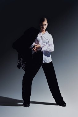 Moda konsepti. Siyah kadife takım elbise ve gri arka planda beyaz gömlekle hareket eden zarif genç bir kadının tam boy portresi.. 