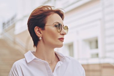 Şehir caddesinde yaz günü gözlüklü, modern orta yaşlı bir kadının portresi. Kadınlar için optik. Yaz stili. 