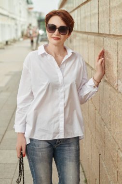 Günümüz orta yaşlı, güneş gözlüklü bir kadının portresi. Bir yaz gününde şehir caddesinde. Kadınlar için optik. Yaz stili. 