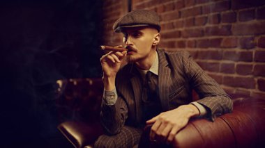 Yakışıklı, cesur bir adamın portresi zengin bir yerde, deri bir kanepede oturmuş puro içiyor. Lüks bir yaşam tarzı. Retro tarzı. Mafya ve suç dünyası, dedektif..