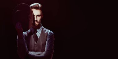 Zarif klasik takım elbiseli cesur yakışıklı bir adam ve bir ışık huzmesi tarafından aydınlatılmış karanlıkta duran bir şapka. Retro tarzı. Lüks. Suç dünyası, mafya..