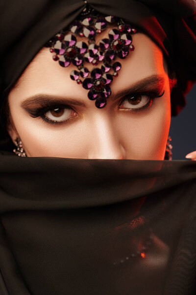 Крупный план портрета красивой восточной женщины с традиционным макияжем, черным хиджабом и украшениями. Макияж и косметика. Арабская красота, мода. 