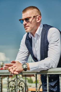 Zarif klasik takım elbiseli mutlu ve olgun bir adam yaz terasında dinleniyor. Erkek modası. Optik, erkekler için güneş gözlüğü. Yaz tatili.