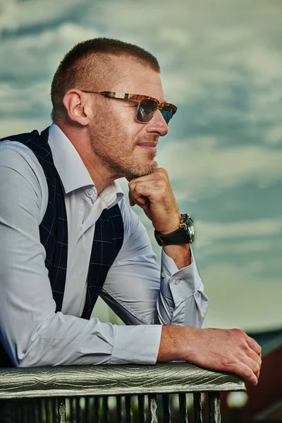Zarif klasik takım elbiseli mutlu ve olgun bir adam yaz terasında dinleniyor. Erkek modası. Optik, erkekler için güneş gözlüğü. Yaz tatili.