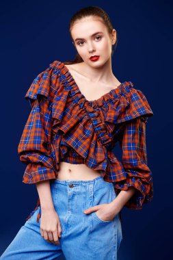 Moda fotoğrafı. Kotla poz veren sevimli bir kız modelinin portresi, koyu mavi arka planda damalı bluz. Country, batı tarzı. Yeni yaz koleksiyonu.