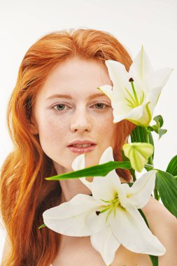 Muhteşem kızıl saçlı, yüzünde çiller ve beyaz zambak çiçekleri olan güzel bir genç kadının portresi. Güzellik, saç ve cilt bakımı. Saç boyası.