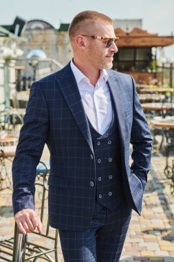Klasik takım elbiseli yakışıklı olgun bir adamın portresi yaz terasında duruyor. Erkek modası. Optik, erkekler için güneş gözlüğü..