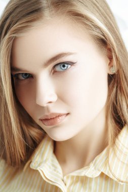 Kameraya bakan, doğal makyajlı ve sarı saçlı güzel bir genç kadının portresi. Beyaz arka planda stüdyo portresi. Kozmetik ürünleri ve makyaj. 