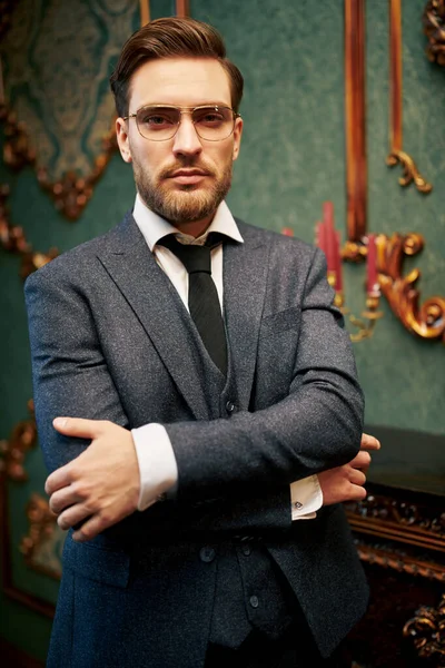 Handsome rich man in elegant suit  stands in a luxurious apartments. Businessman portrait. Man's fashion.
