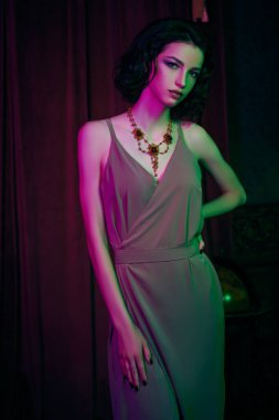 Çekici esmer kadın, akşam makyajı ve saç stiliyle lüks bir dairede şık bir şekilde poz veriyor. Kırmızı ve yeşil ışıkta. Moda fotoğrafı.. 