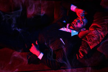 Lüks bir dairede, kanepede uzanmış yakışıklı bir esmer adamın portresi. Göz kamaştırıcı bir yaşam tarzı. Moda fotoğrafı. Erkek kıyafetleri ve aksesuarları..