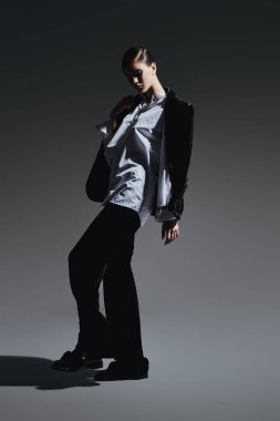 Moda konsepti. Siyah kadife takım elbise ve gri arka planda beyaz gömlekle hareket eden zarif genç bir kadının tam boy portresi.. 