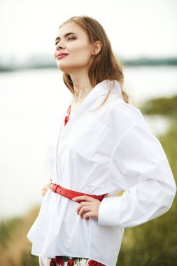 Açık beyaz gömlekli güzel romantik kız nehir kıyısında duruyor ve gülümsüyor. Mutlu yaz tatilleri..