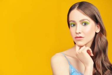 Makyaj ve makyaj malzemeleri. Sarı arka planda parlak renkli makyajlı, gülümseyen güzel bir kızın portresi. Boşluğu kopyala.