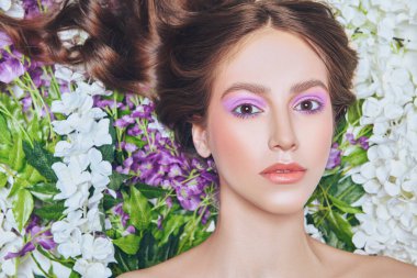 Bahar ve yaz güzelliği. Uzun dalgalı saçlı ve çiçekli renkli makyajlı hassas bir genç kadının portresi. Makyaj ve kozmetik.