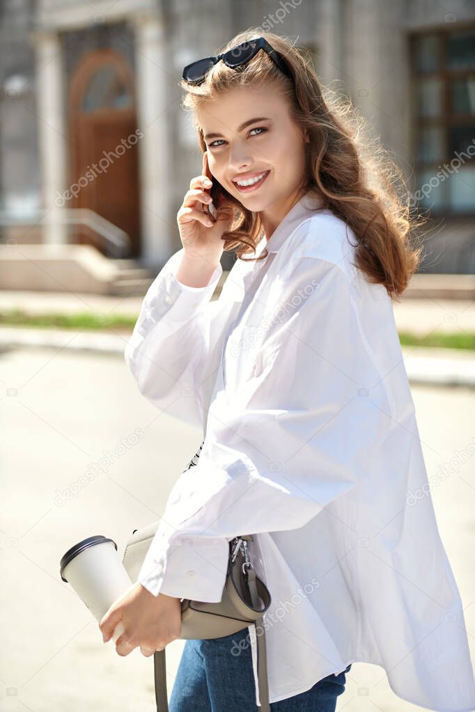 Beautiful happy girl walks around the city and talks on her phone on a sunny summer day. Summer vacation, trips. Happy people concept.