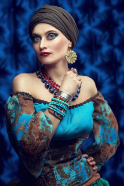 Koyu mavi arka planda güzel bir çingene kadının portresi. Ulusal çingene kostümü, etnik. Makyaj ve başlık.