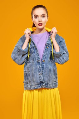 Modern gençlik görünüşü. Kot ceketli, sarı renkli genç ve duygusal bir kız modern güneş gözlükleriyle sarı arka planda poz veriyor. Güzellik, moda.