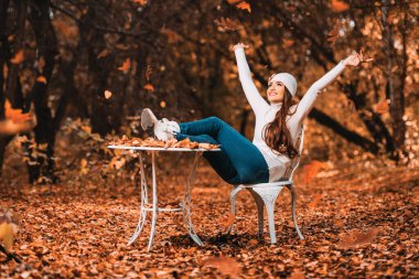 Sonbahar bahçesindeki bir masada oturan güzel genç bir kadın. Yaşam tarzı, sonbahar modası, güzellik. 