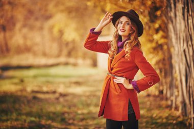Güzel genç bir kadın sonbahar parkında yürüyor ve gülümsüyor. Sonbahar güzelliği, moda.
