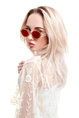 Yaz stili. Açık beyaz dantelli elbise ve güneş gözlüğü takan sarışın güzel bir kızın portresi. Beyaz arkaplanda stüdyo portresi.