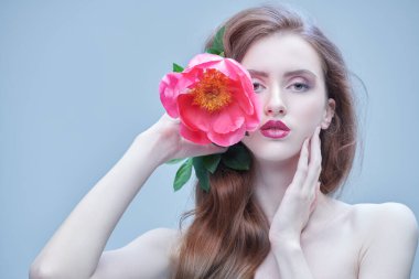 Beyaz elbiseli çekici, esmer bir kadın. Şakayık çiçeğiyle poz veriyor. Güzellik, moda portresi. Makyaj ve makyaj malzemeleri. Düğün stili.