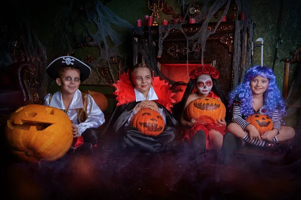 Halloween. Funny kids in carnival costumes are sitting with pumpkins the old castle on Halloween.