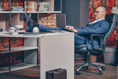 Takım elbiseli ve gözlüklü saygıdeğer orta yaşlı işadamı modern bir ofiste çalışıyor. Başarılı yönetici kavramı.