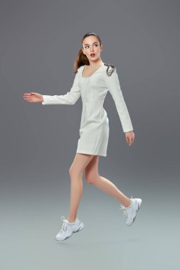 Moda fotoğrafı. Gri arka planda koşan beyaz elbiseli güzel bir genç kadının portresi. Mavi akuamarin göz oklarıyla modaya uygun makyaj. Makyaj ve kozmetik. 