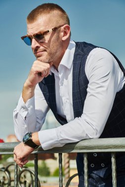 Zarif klasik takım elbiseli yakışıklı olgun bir adam yaz terasında dinleniyor. Erkek modası. Optik, erkekler için güneş gözlüğü. Yaz tatili.