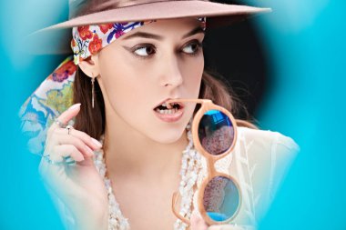 Mavi çerçeveli siyah bir arka planda şapka ve güneş gözlüğü takan modern bir kızın portresi. Yaz modası. Boho, modern hippi tarzı..