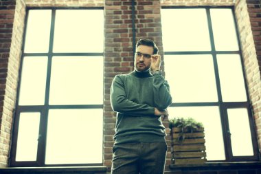 İş konsepti. Pencerelerin arkasında duran yakışıklı, ciddi bir adamın portresi. Erkek güzelliği, moda. 