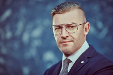 Mavi arka planda gözlüklü ve takım elbiseli saygıdeğer olgun bir adamın portresi. İş adamı portresi. Boşluğu kopyala.